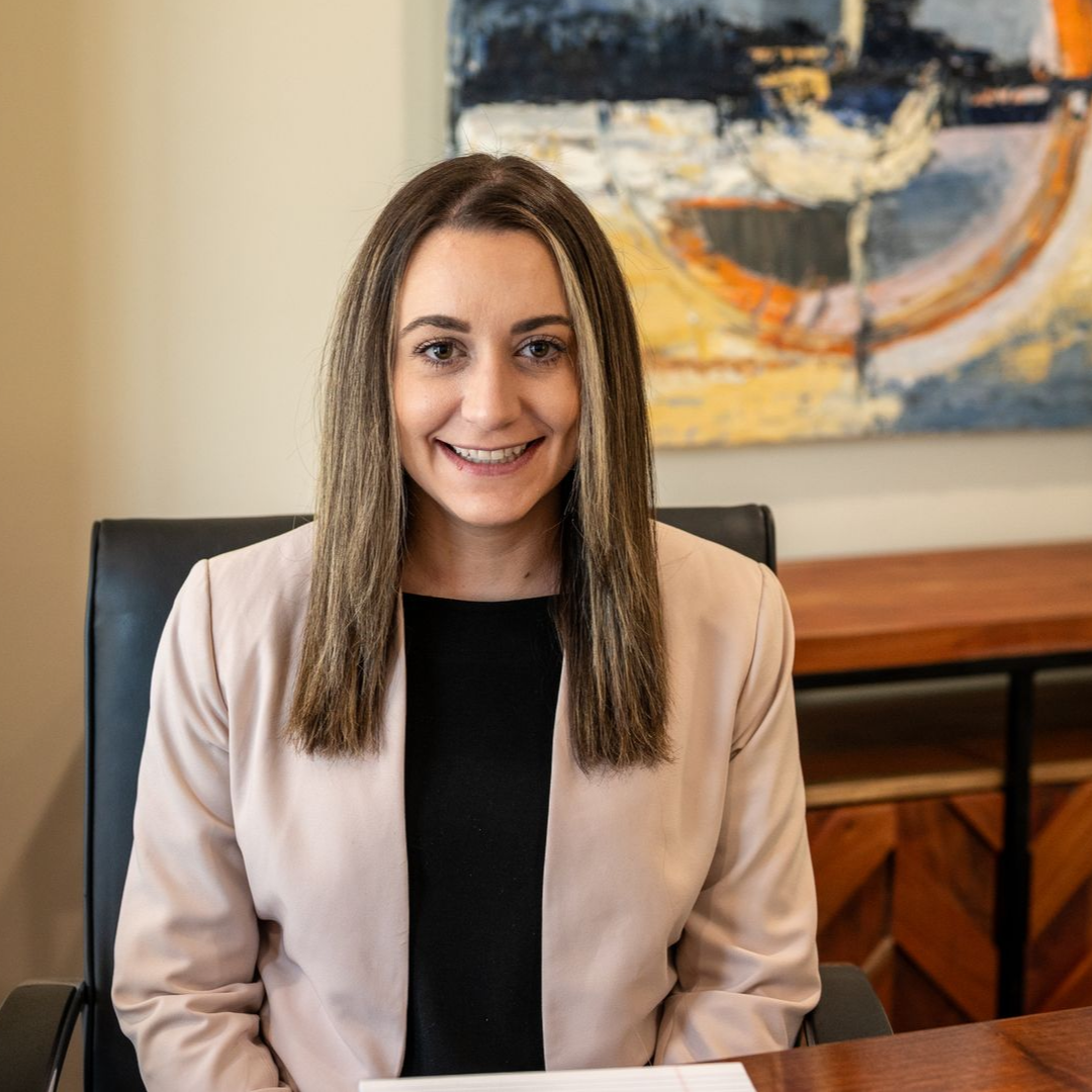 Corrine Curcio of Delaware Wealth Planners at a desk in a beige blazer, with abstract wall art in the background