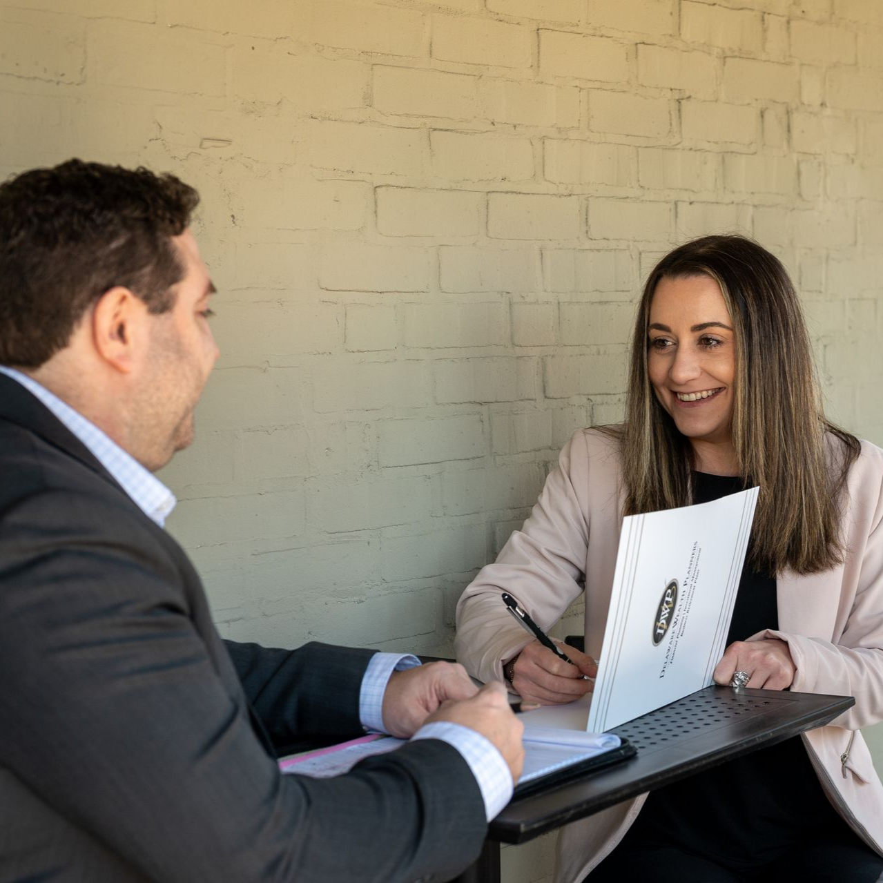Brent Bonstingl and Corrine Curcio of Delaware Wealth Planners in a meeting across a table, smiling and reviewing a laptop and documents.