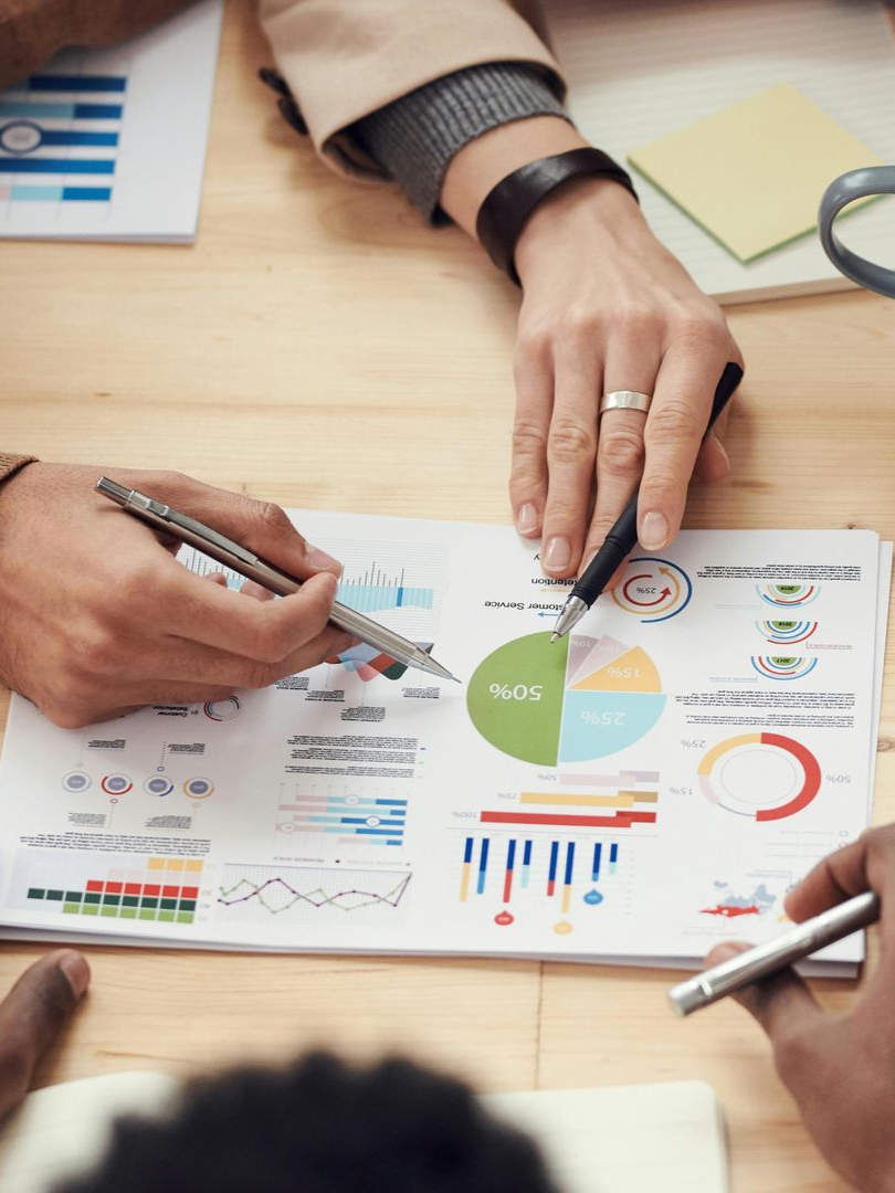 Hands reviewing printed charts and graphs around a table, with pens and papers in a business meeting.