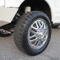 Close-up of a truck’s front wheel with chrome rim and rugged off-road tire on pavement