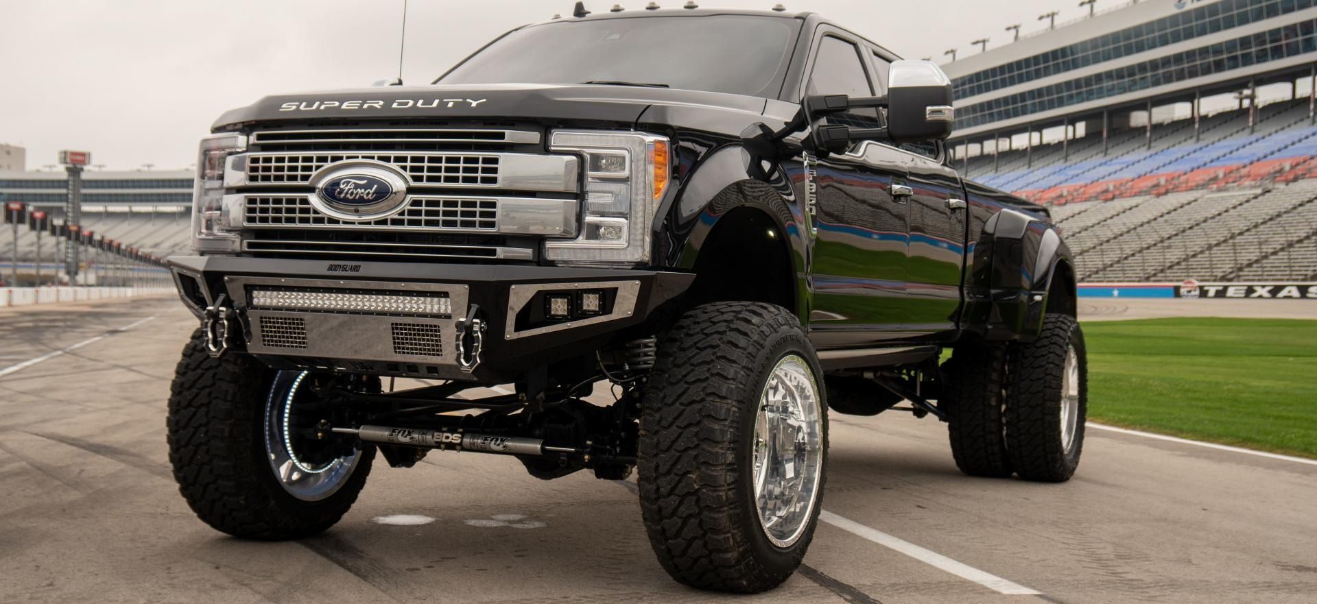 Black lifted Ford truck on a racetrack, front three-quarter view