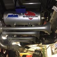 Undercarriage of a car with a large silver aftermarket exhaust system and muffler installed.