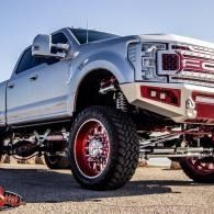 Lifted silver pickup truck with oversized red wheels, parked outdoors.