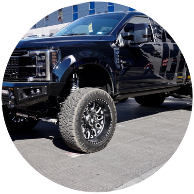 Black lifted pickup truck with oversized off-road tires parked outdoors in sunlight