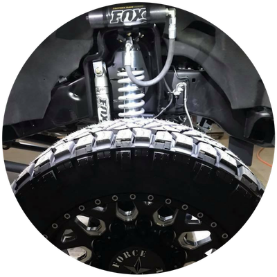 Close-up of off-road truck suspension and large treaded tire with black wheel and silver coilover shock