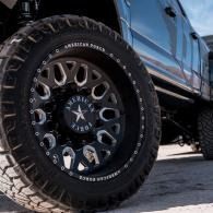 Close-up of a black off-road truck tire with star-pattern rim and rugged tread on pavement