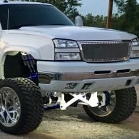White lifted SUV with oversized off-road tires parked on gravel outdoors