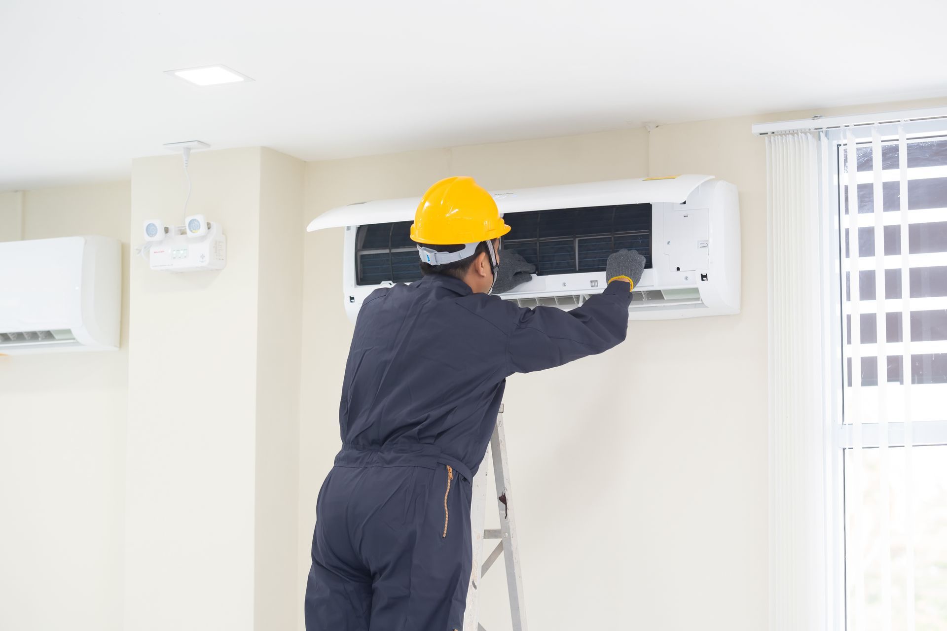 An air conditioning repair contractor fixing an air conditioner in a blue shirt and gloves.