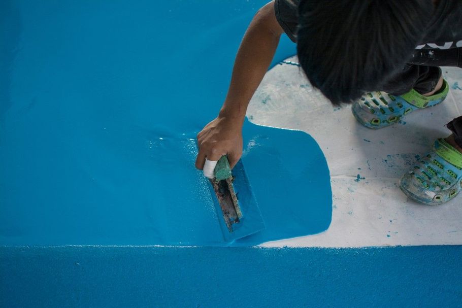 Person painting a blue wall edge with a brush, touching up white trim