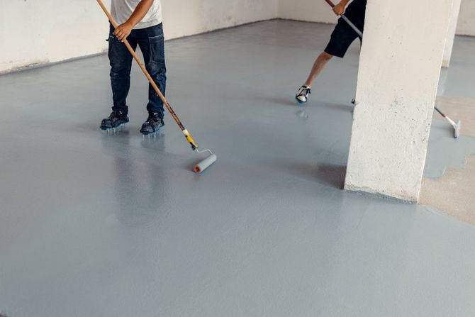 Two people rolling gray epoxy flooring in a room with white columns