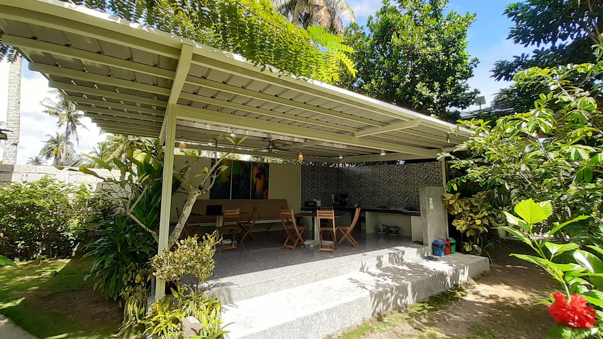 Covered patio with seating and an outdoor kitchen surrounded by lush greenery.
