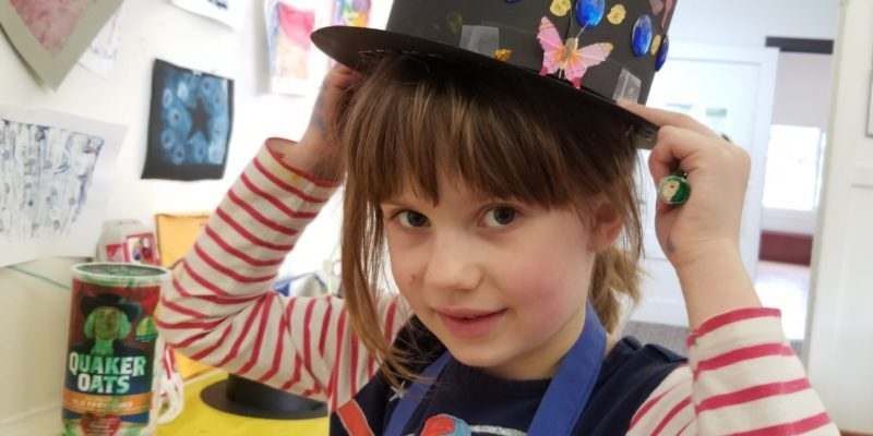 A little girl wearing a top hat with butterflies on it