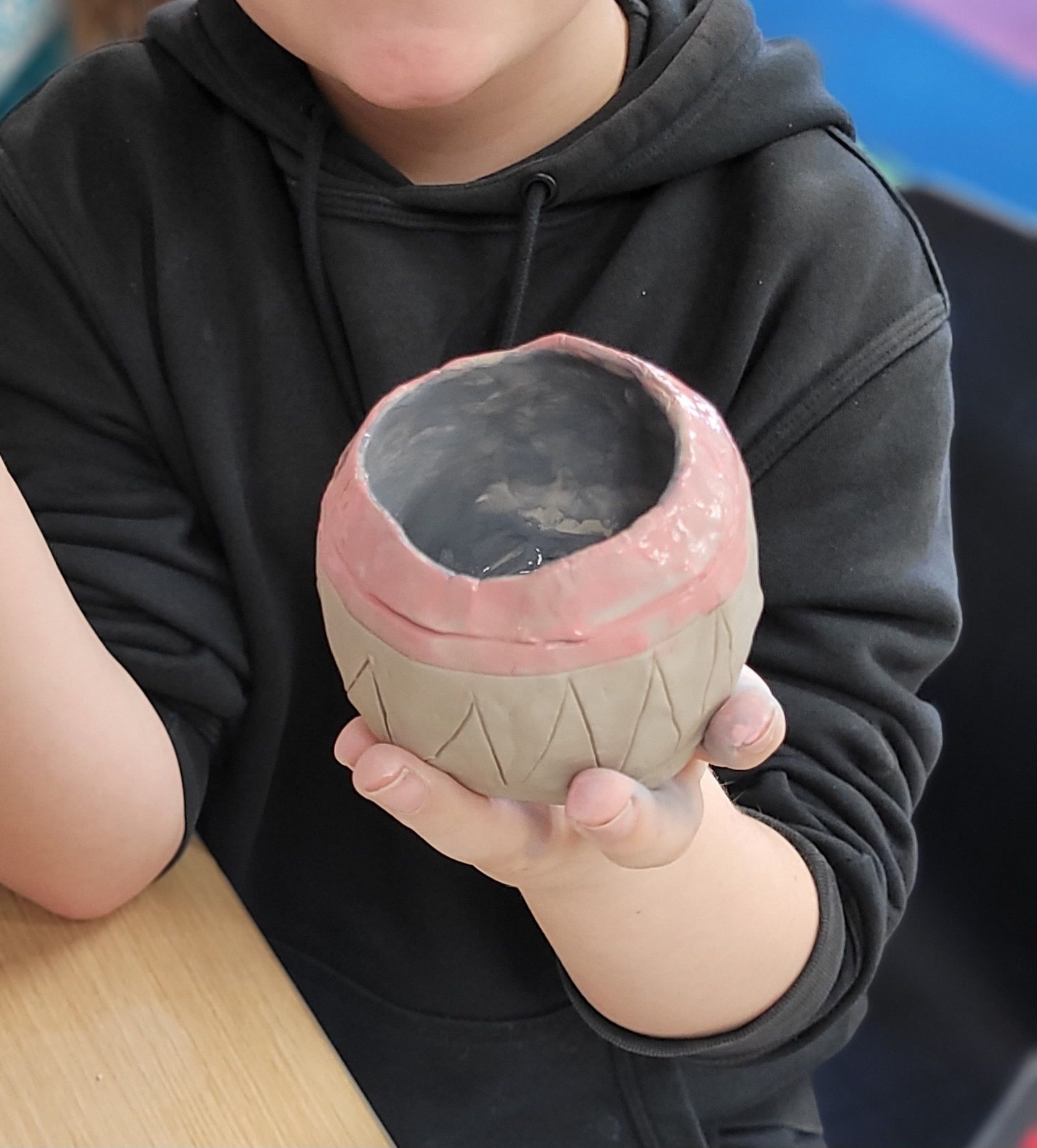 A person in a black hoodie is holding a clay pot