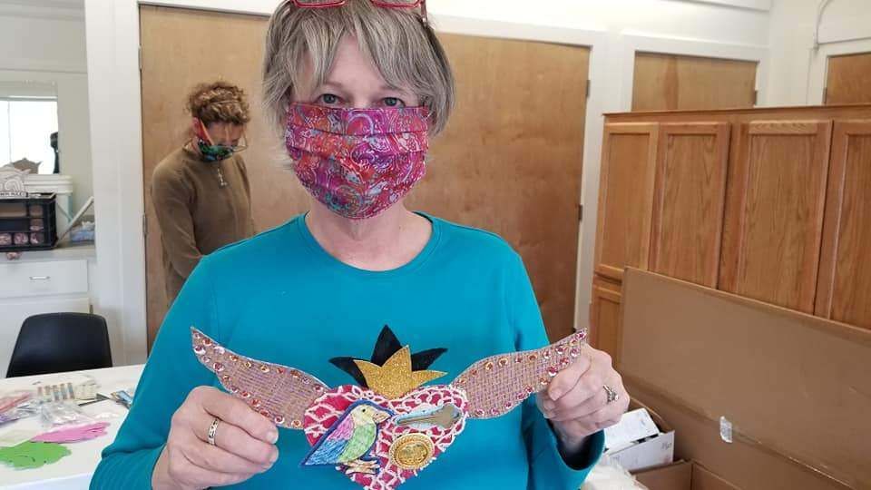 A woman wearing a mask is holding a heart with wings.