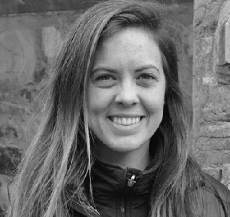 A black and white photo of a woman smiling in front of a brick wall.