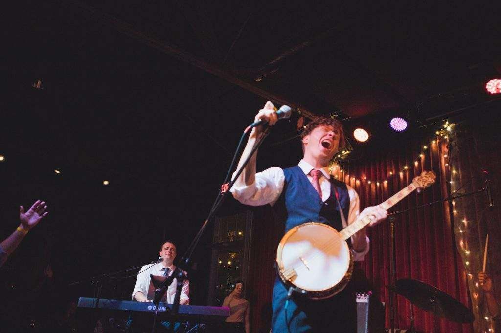 A man is playing a banjo and singing into a microphone on a stage.