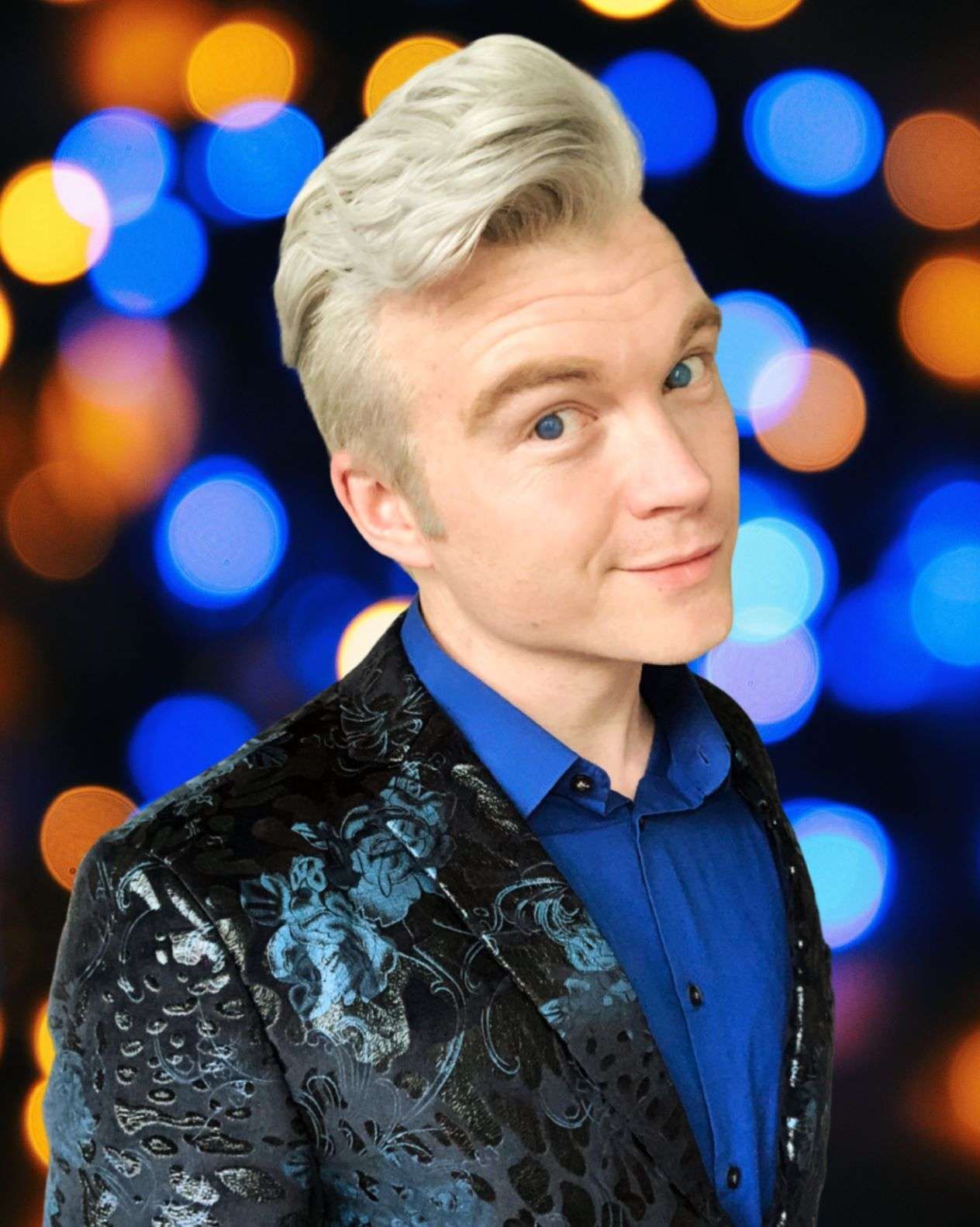 A man with blonde hair is wearing a blue shirt and a black jacket.