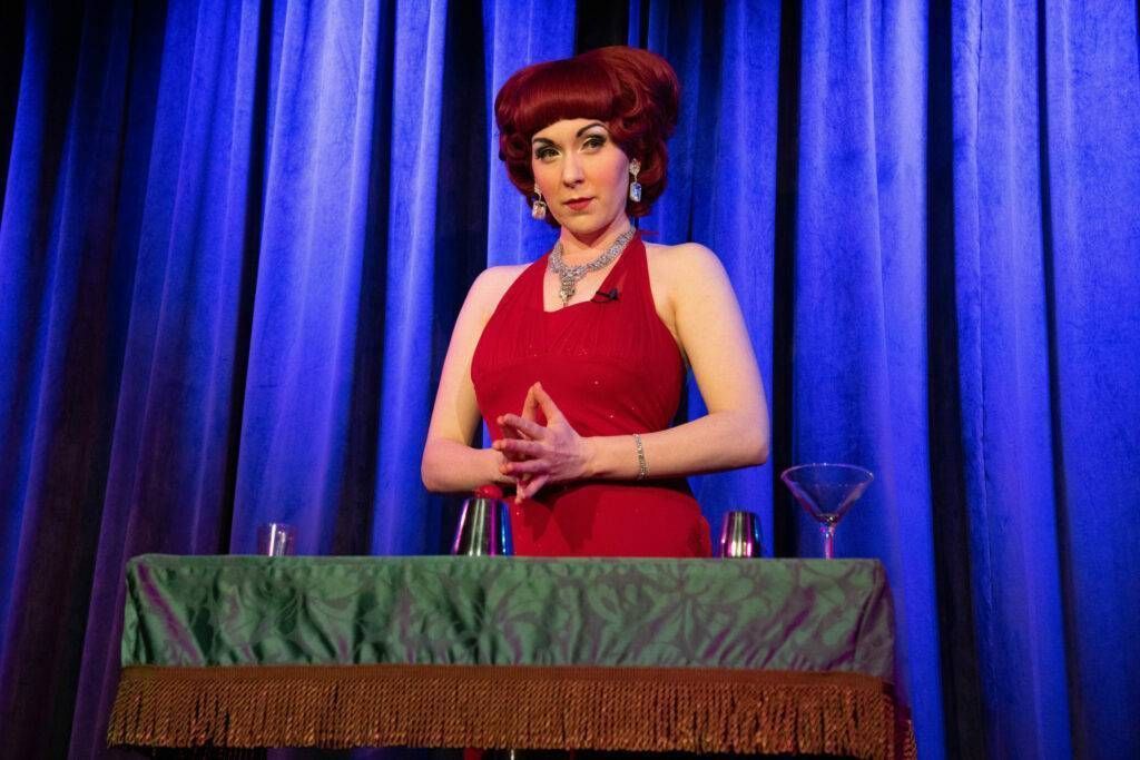 A woman in a red dress is standing at a table with a martini glass.
