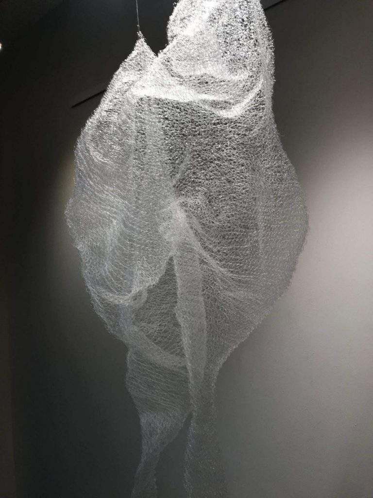 A sculpture of a woman is hanging from the ceiling in a room.