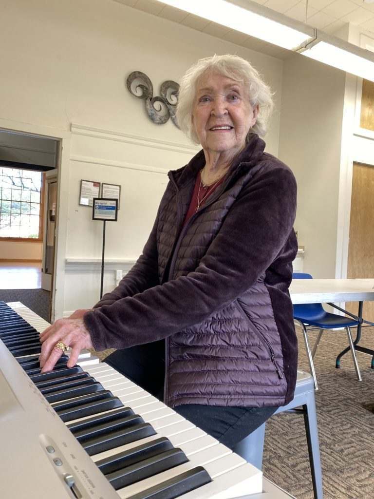 An elderly woman is playing a piano in a room.