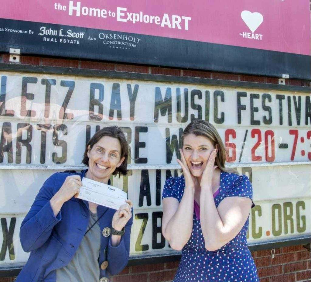 Two women standing in front of a sign that says letz bay music festival
