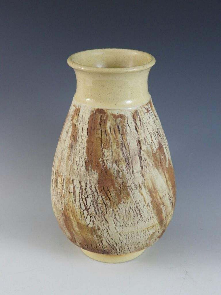 A brown and white vase is sitting on a white surface.