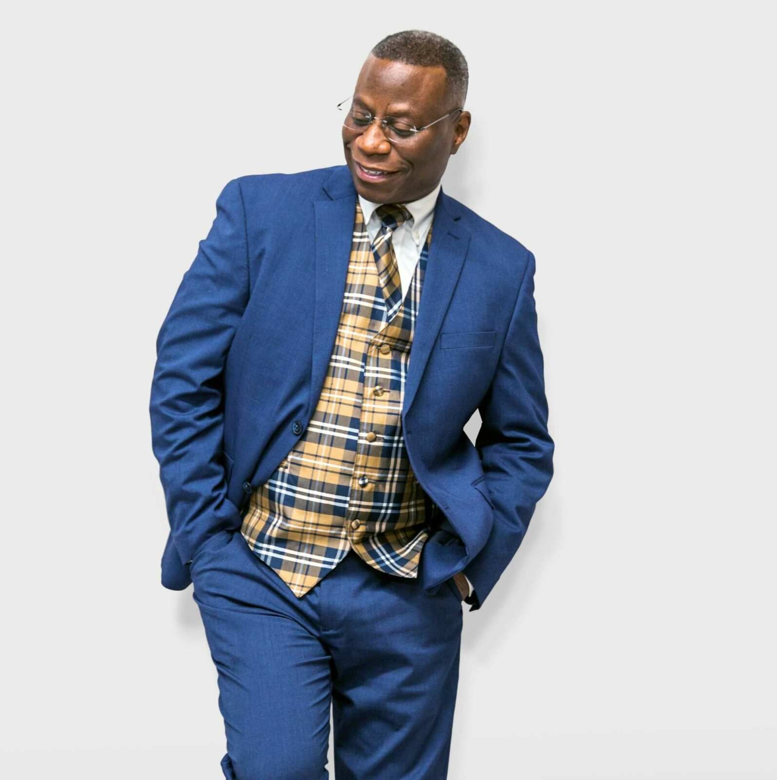 A man in a blue suit and plaid vest is standing with his hands in his pockets