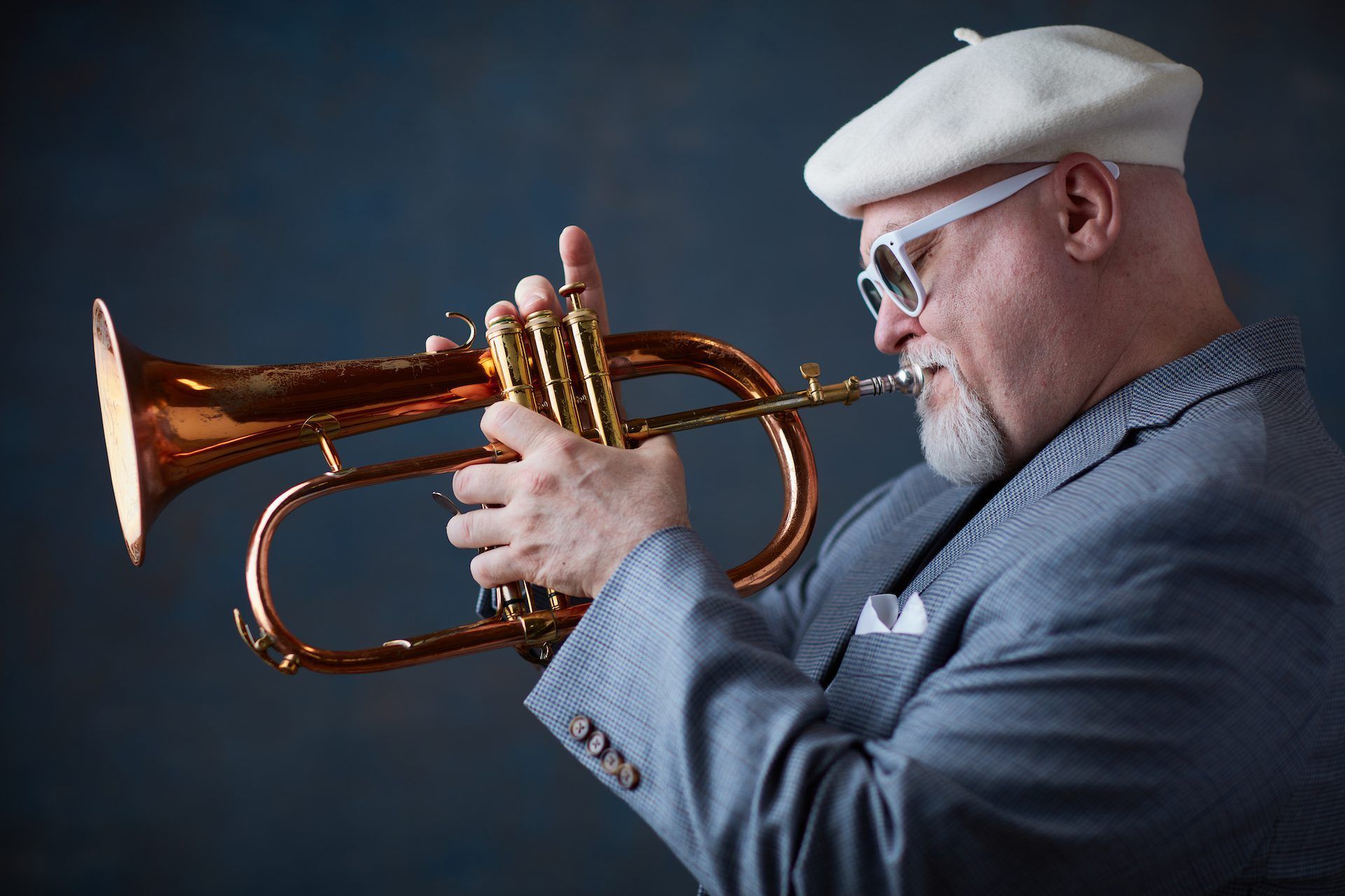 A man wearing a white beret and sunglasses is playing a trumpet.