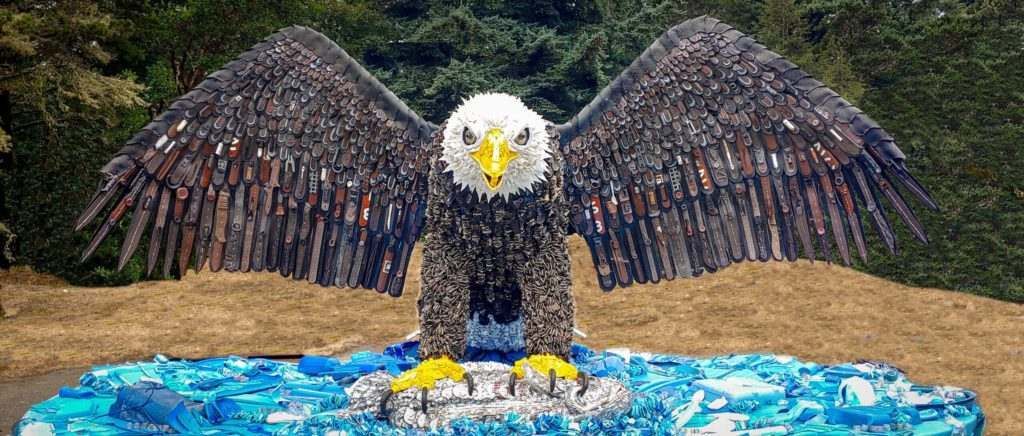A bald eagle made out of plastic bottles is sitting on a blue surface.