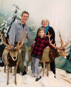 A family is posing for a picture with reindeer in the snow.