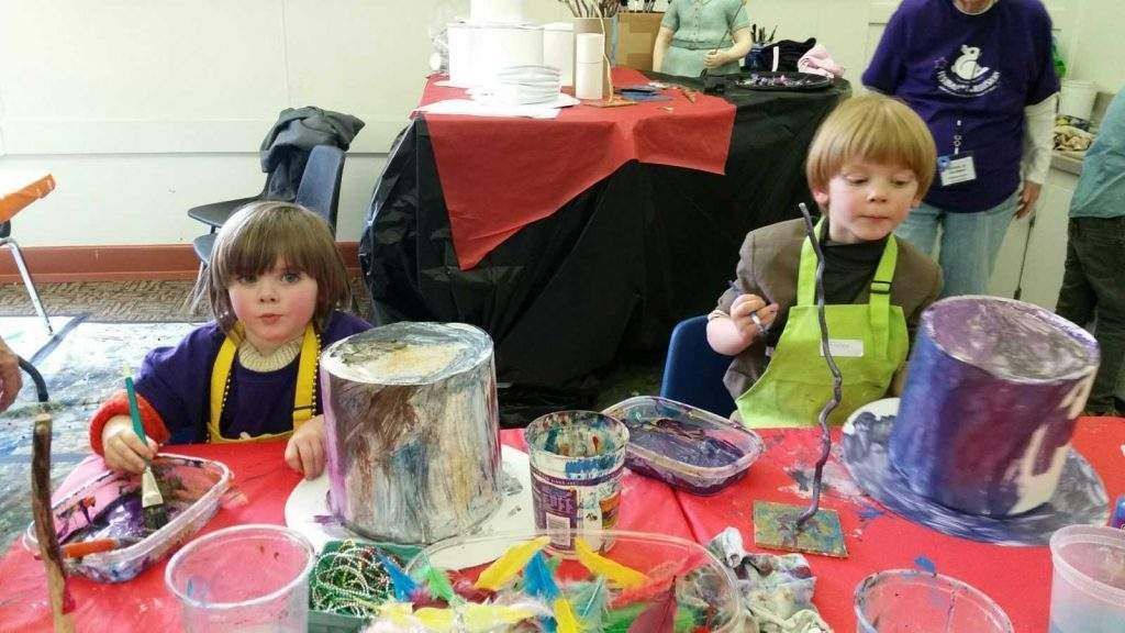 Two children are sitting at a table with buckets of paint