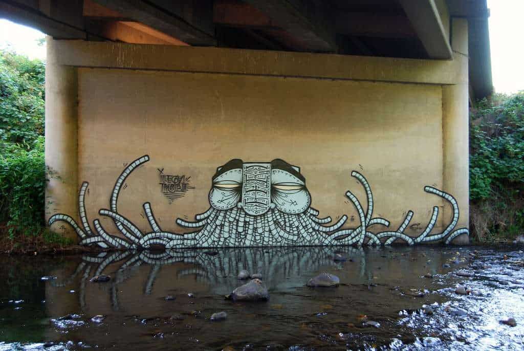 A wall with graffiti on it under a bridge over a river.