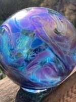 A purple and blue glass ball is sitting on a rock.