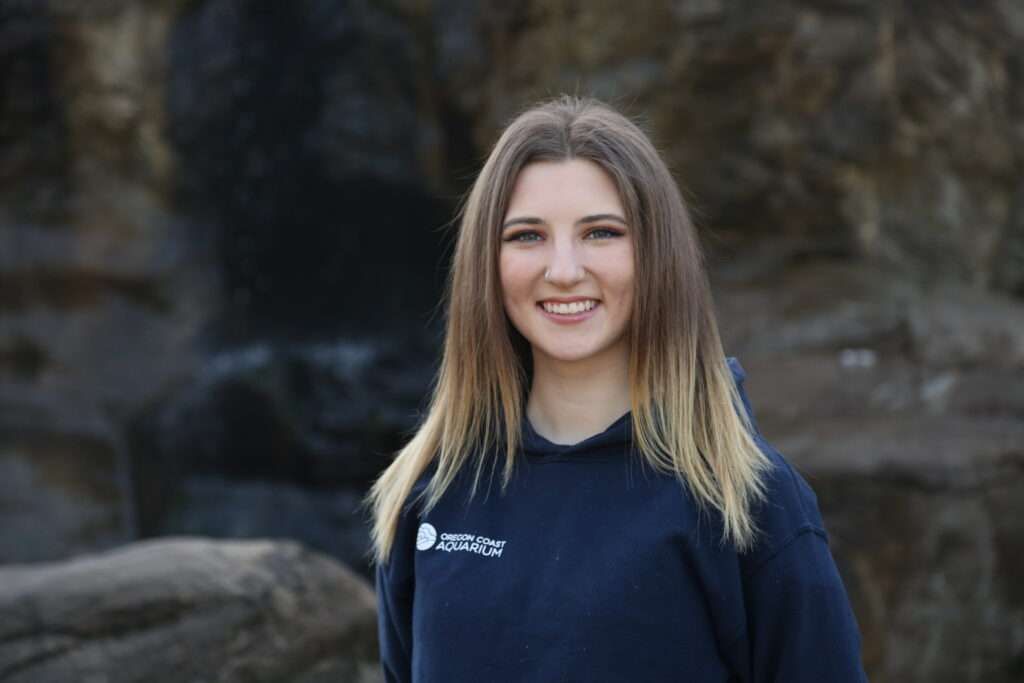 A woman in a blue hoodie is standing in front of a waterfall.