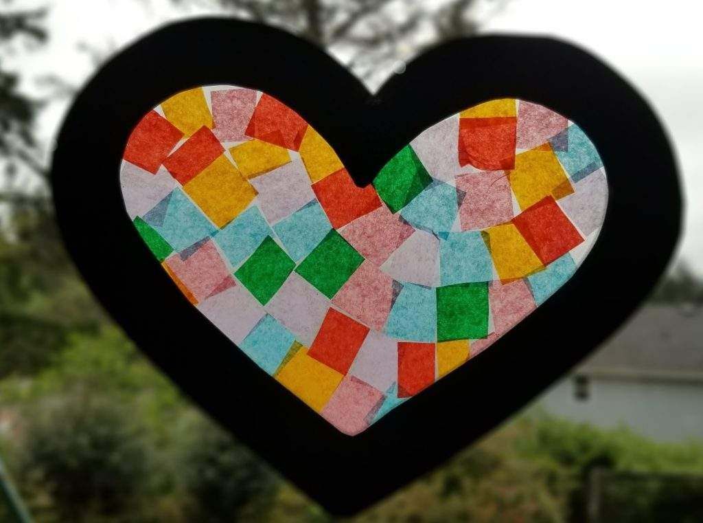 A heart made out of colorful squares is hanging on a window