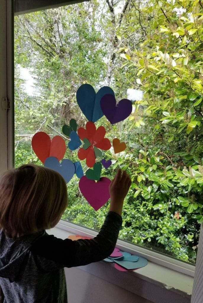 A little girl is looking out of a window with hearts and flowers on it.