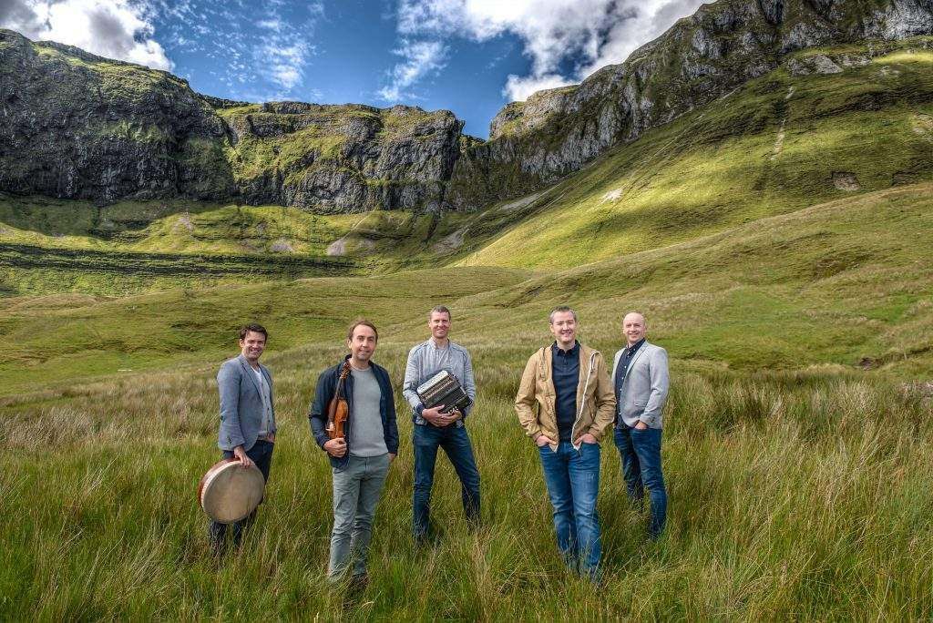 A group of men are standing in a grassy field in front of a mountain.