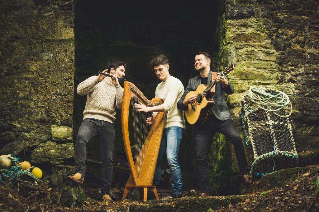 Three men are standing next to each other playing harps and guitars.