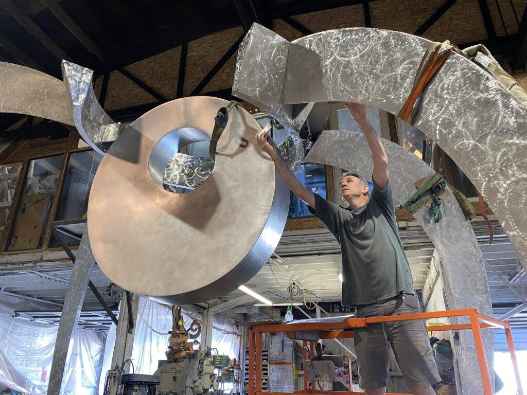 A man is working on a large metal sculpture in a factory.