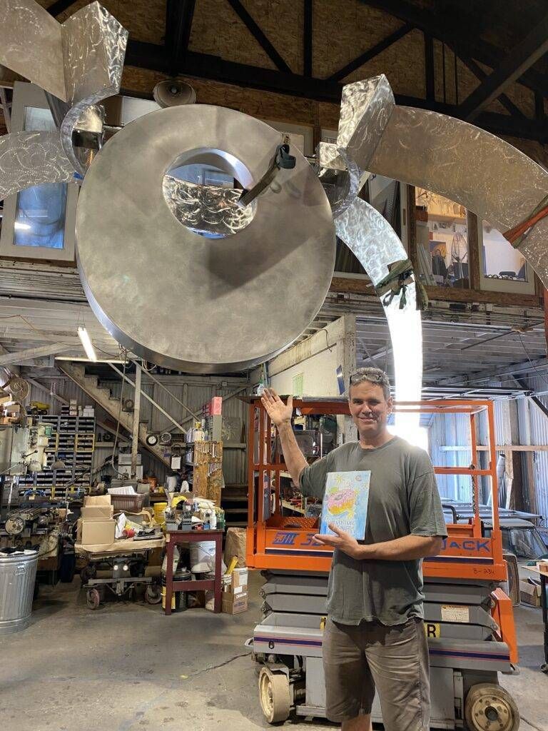 A man is standing in front of a large metal object in a factory holding a book.