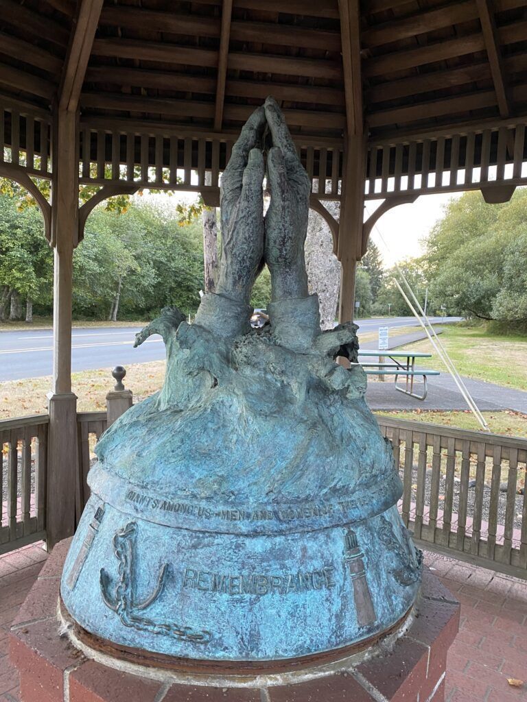 A statue of two hands praying under a gazebo in a park.
