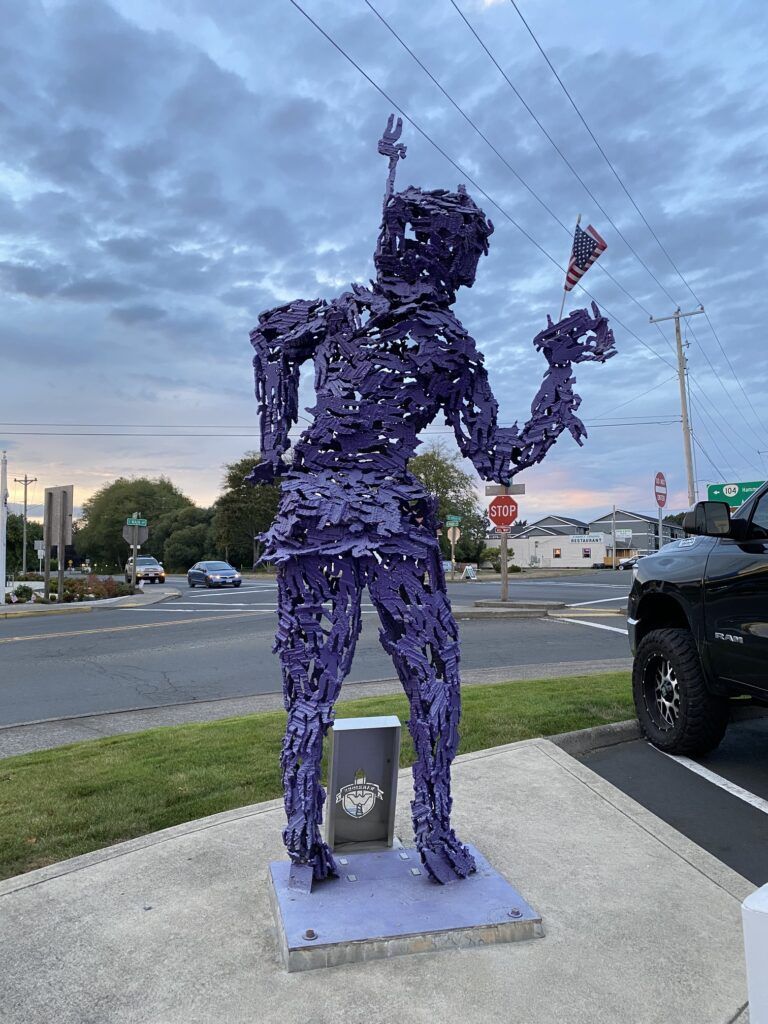 A purple statue of a man is standing in a parking lot.