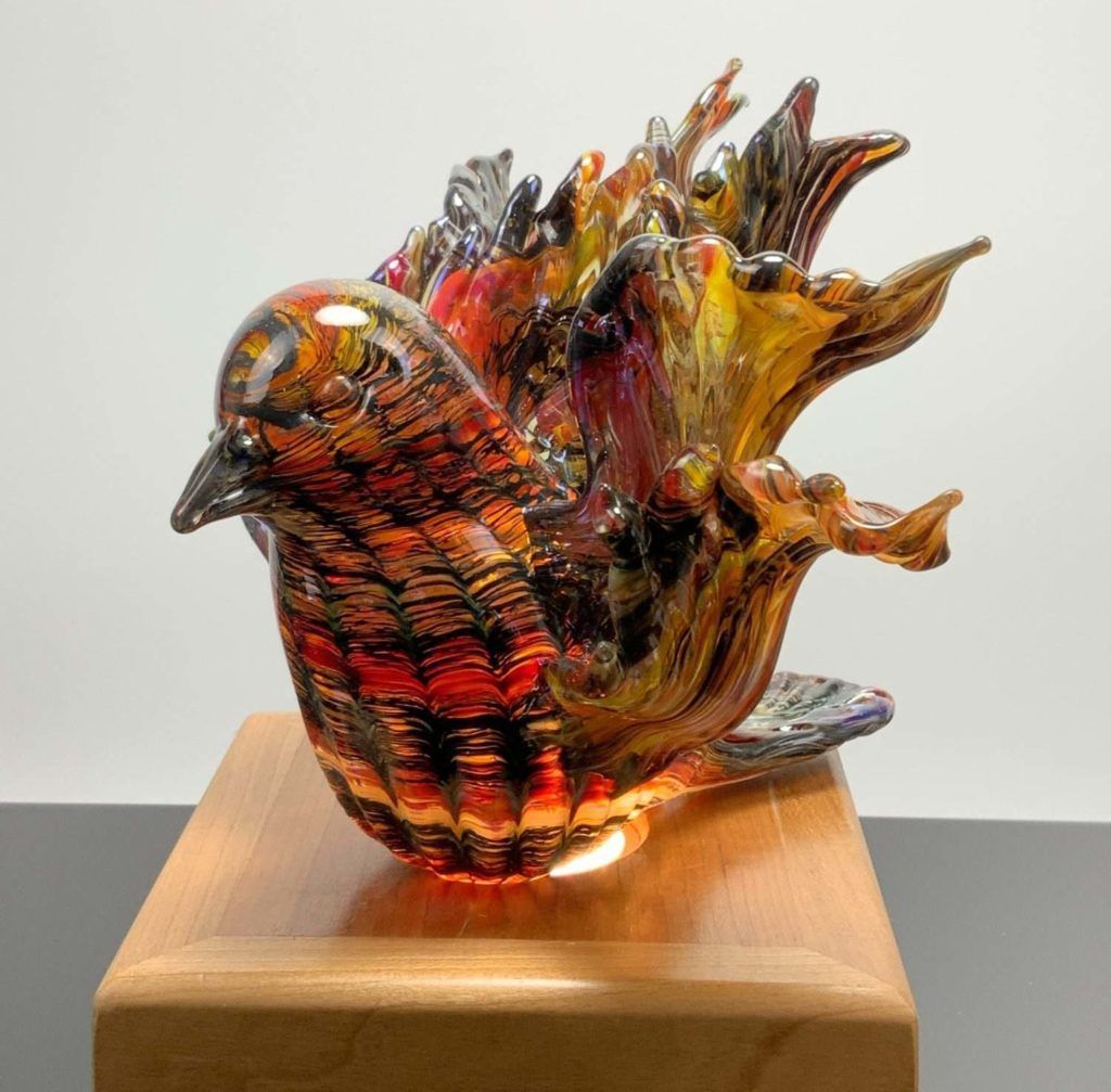A colorful glass bird is sitting on a wooden base