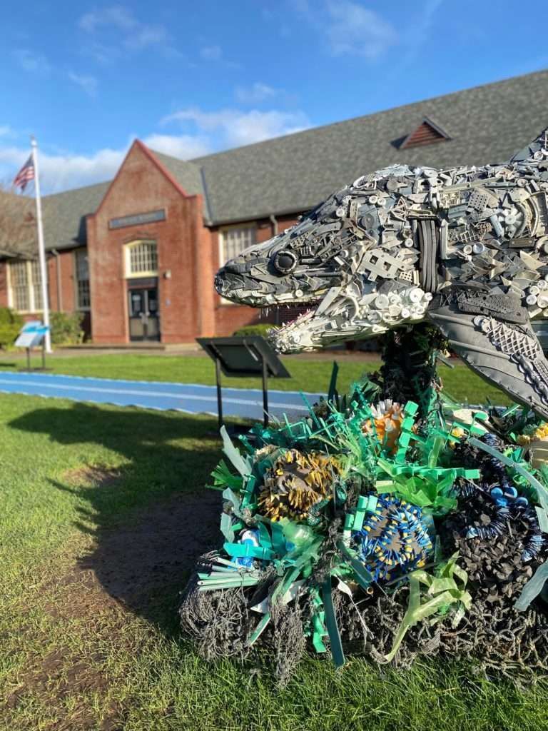 A statue of a turtle made out of plastic bottles is in front of a building.