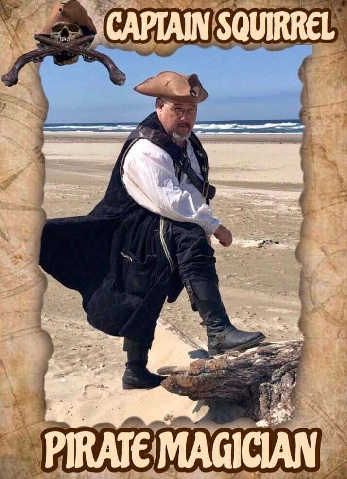 A man dressed as a pirate is standing on a rock on the beach.