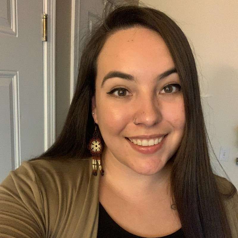 A woman is smiling for the camera while wearing a cardigan and earrings.