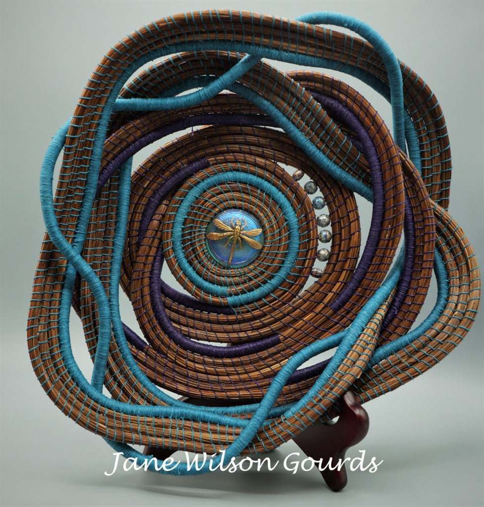 A sculpture made by jane wilson gourds is sitting on a wooden stand