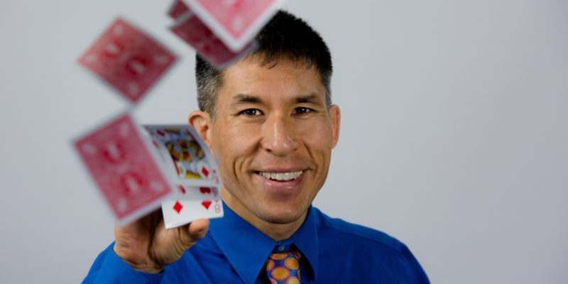 A man in a blue shirt and tie is throwing playing cards in the air.
