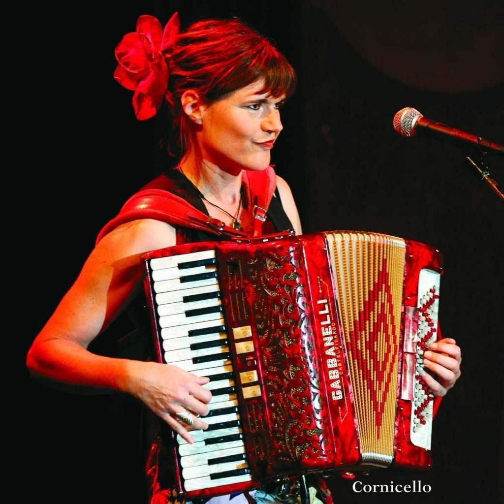 A woman is playing a red accordion and singing into a microphone