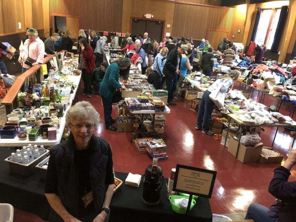 A woman is sitting in front of a table at a flea market.